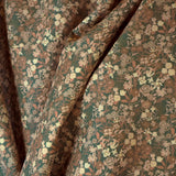 Draped fabric yardage in a dense small-scale floral print in shades of brown and tan on a green field.