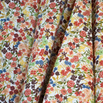 Draped fabric yardage in a dense small-scale floral print in shades of coral, red, green and blue on a white field.