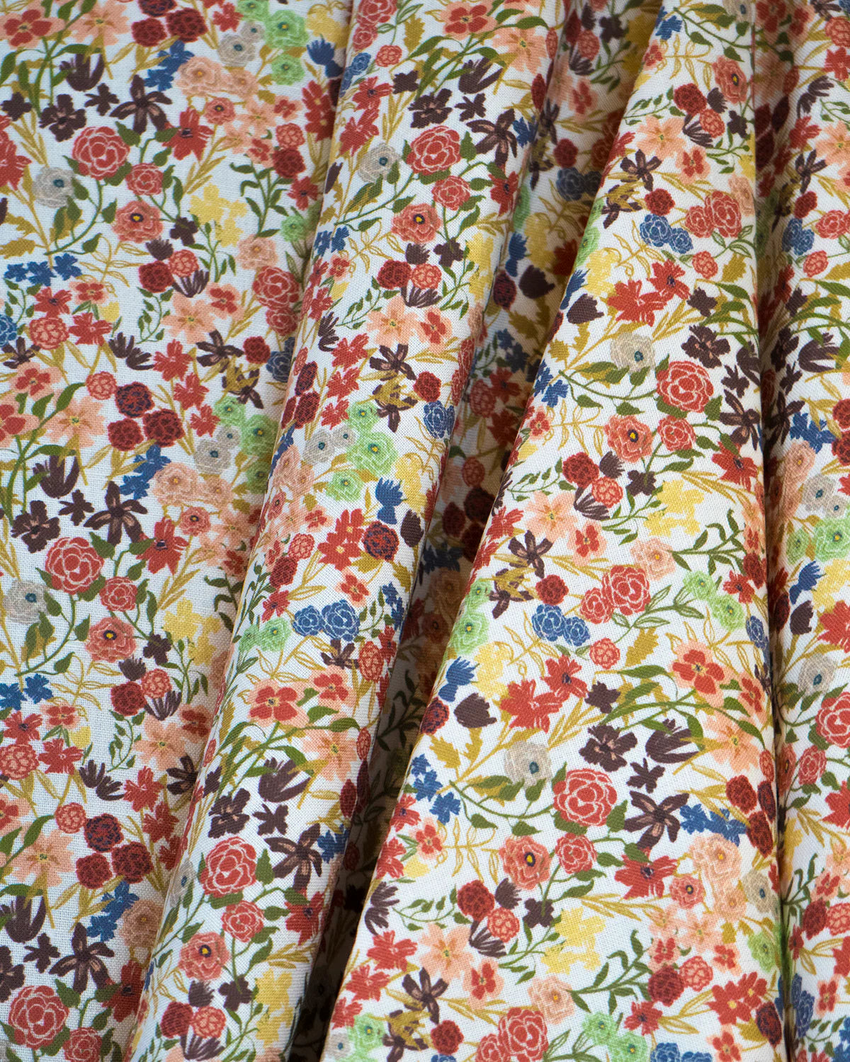 Draped fabric yardage in a dense small-scale floral print in shades of coral, red, green and blue on a white field.