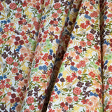 Draped fabric yardage in a dense small-scale floral print in shades of coral, red, green and blue on a white field.