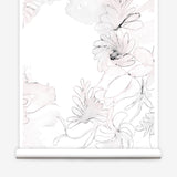 Partially unrolled wallpaper yardage in a painterly floral print in shades of pink and charcoal on a white field.