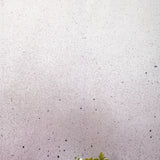 Two vases of flowers stand in front of a wall covered in an abstract ombré paint splatter print in purple, gray and white.