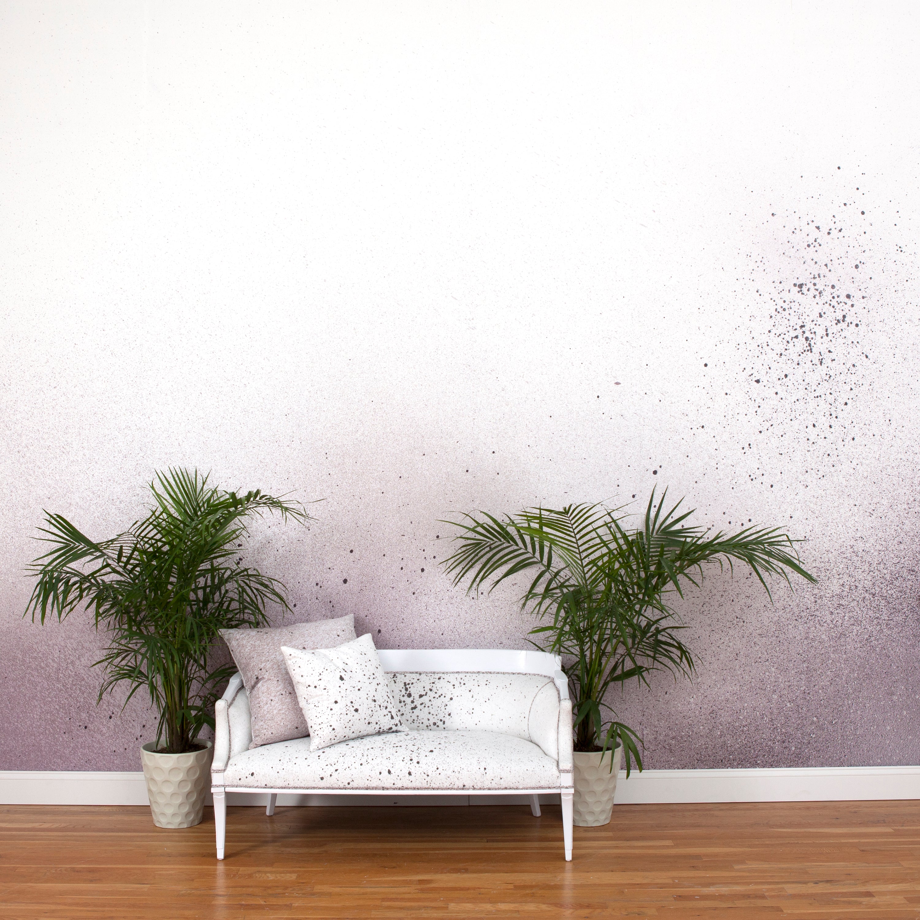 A sofa and potted plants stands in an abstract ombré paint splatter print in shades of purple, gray and white.