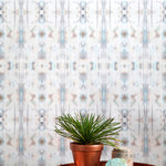 A plant and some crystals stand in front of a wall papered in a painterly ikat print in turquoise, gray and tan.