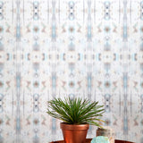 A plant and some crystals stand in front of a wall papered in a painterly ikat print in turquoise, gray and tan.
