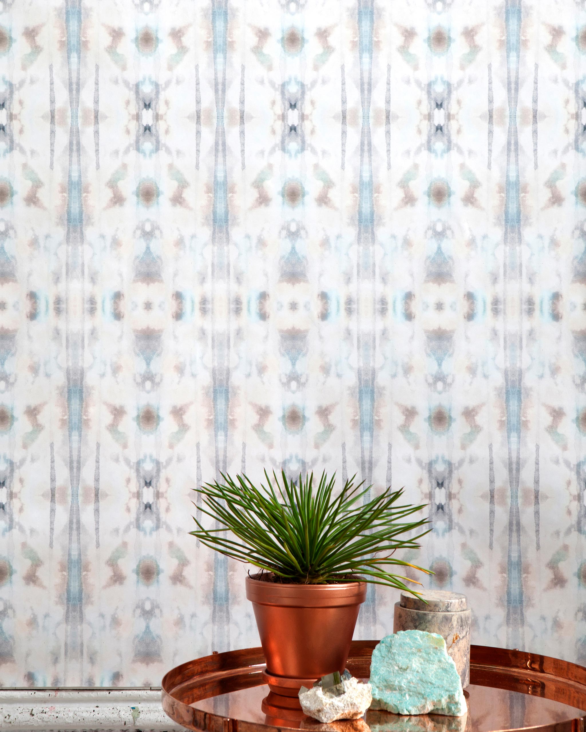 A plant and some crystals stand in front of a wall papered in a painterly ikat print in turquoise, gray and tan.