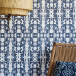 A lamp and statement chair stand in front of a wall papered in a painterly ikat print in navy and white.