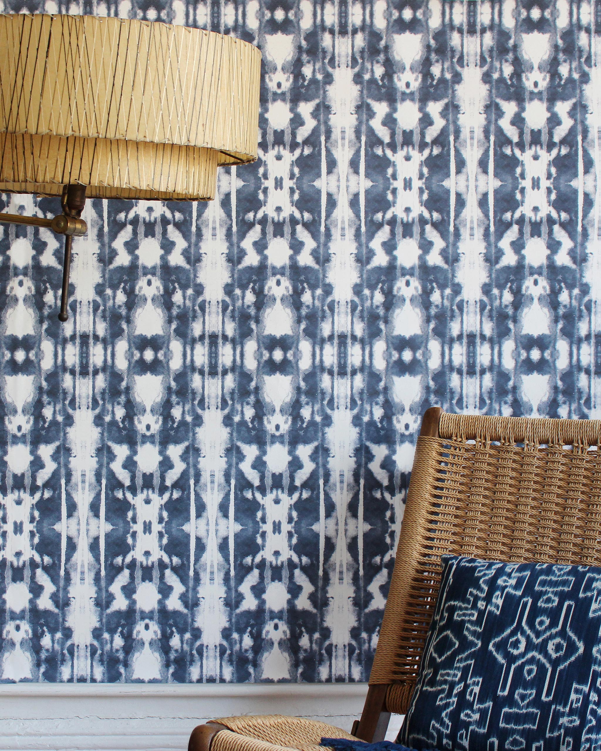 A lamp and statement chair stand in front of a wall papered in a painterly ikat print in navy and white.