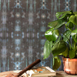 A house plant, some books and a hammer stand in front of a wall papered in a painterly ikat print in turquoise and brown.