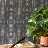 A house plant, some books and a hammer stand in front of a wall papered in a painterly ikat print in turquoise and brown.