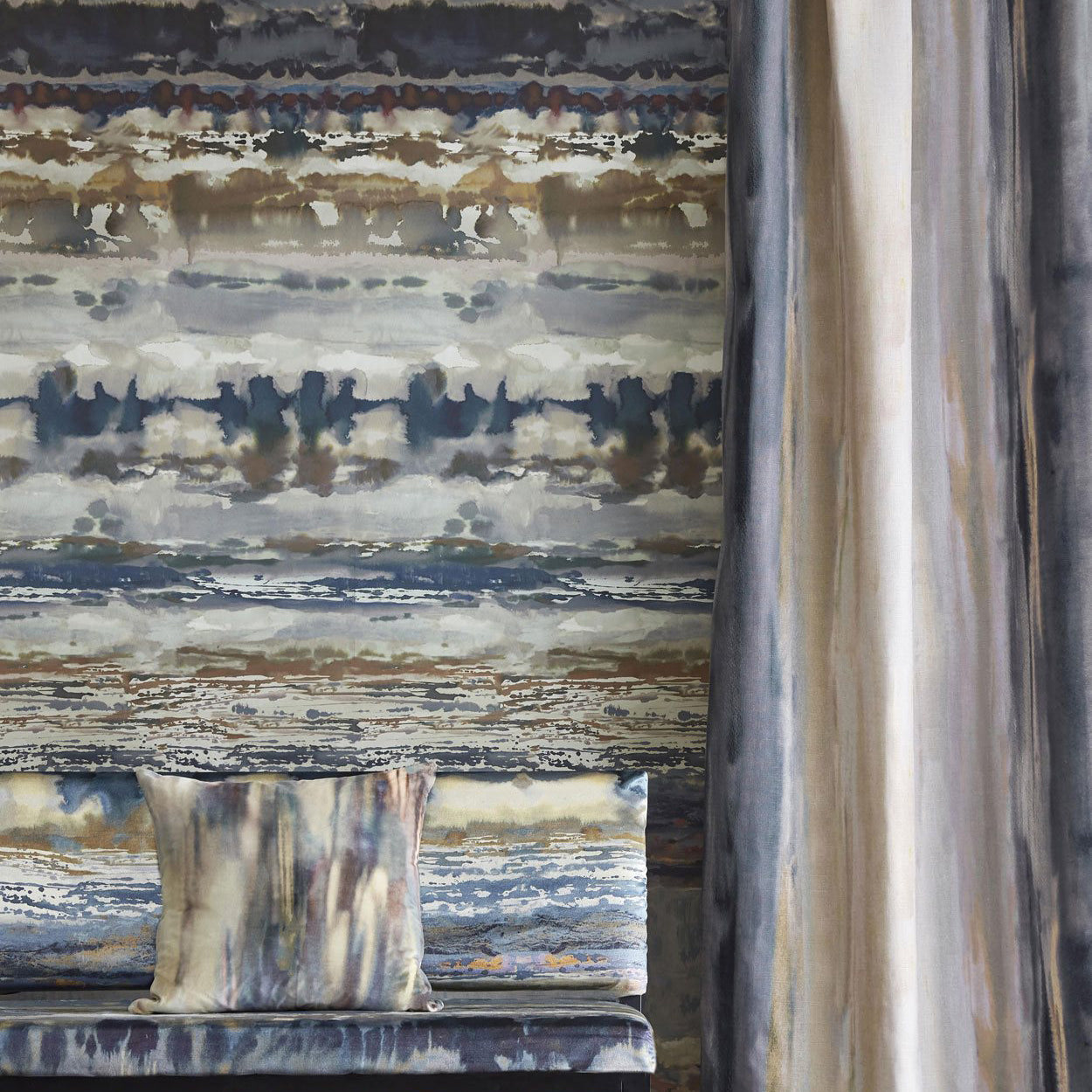 A room with a long curtain, bench and pillow, all covered in the same painterly stripe in shades of blue, green, mauve and gray.