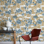 A modernist armchair stands in front of a wall papered in a painterly palm tree print in shades of gray, brown and navy.