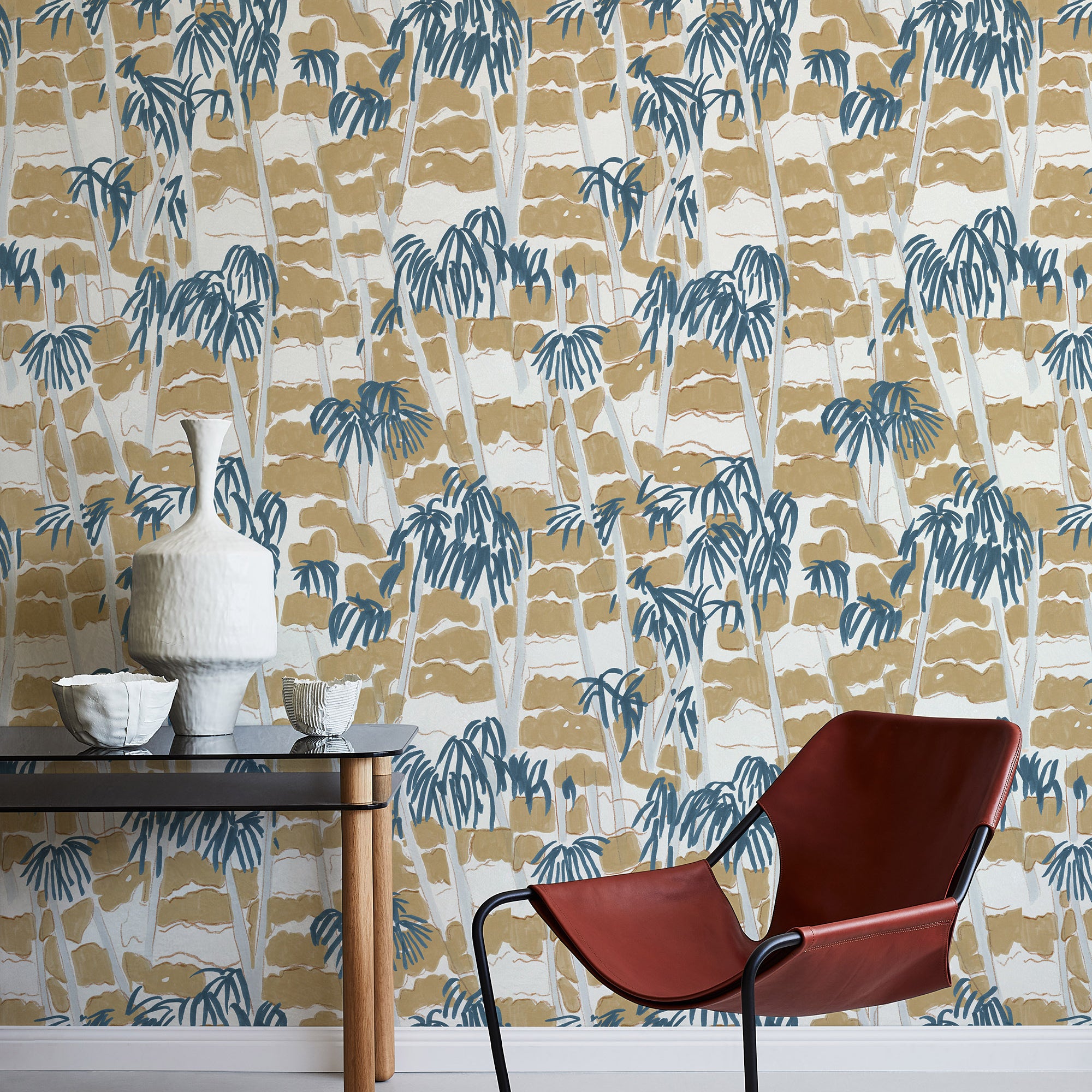 A modernist armchair stands in front of a wall papered in a painterly palm tree print in shades of gray, brown and navy.