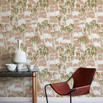 A modernist armchair stands in front of a wall papered in a painterly palm tree print in shades of pink, beige and olive.