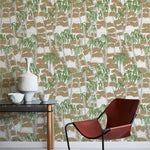 A modernist armchair stands in front of a wall papered in a painterly palm tree print in shades of green, gray and brown.