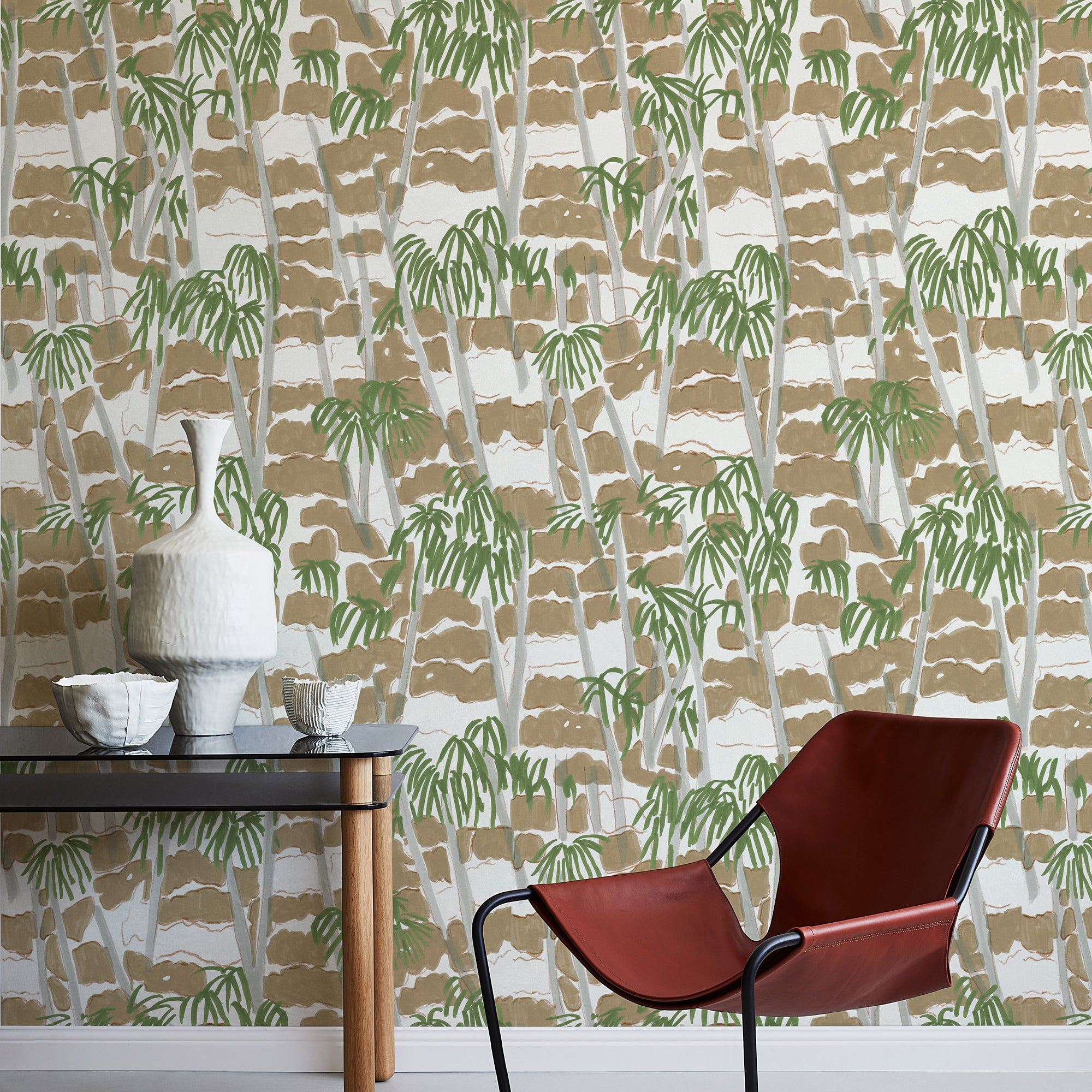 A modernist armchair stands in front of a wall papered in a painterly palm tree print in shades of green, gray and brown.