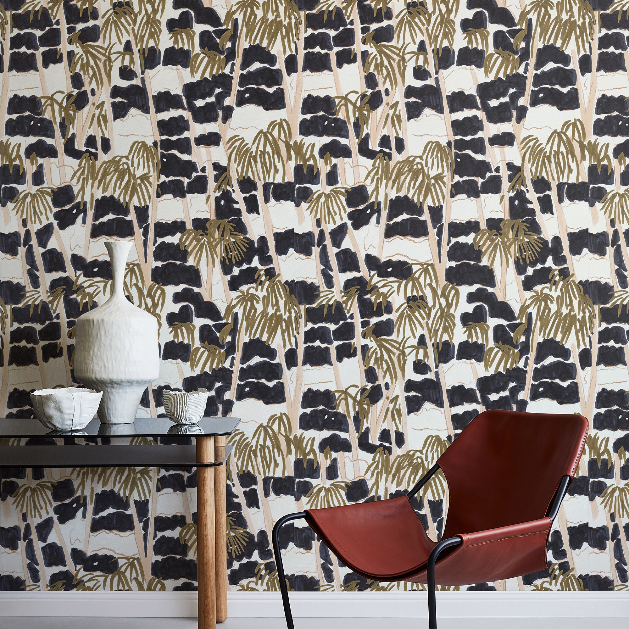 A modernist armchair stands in front of a wall papered in a painterly palm tree print in shades of gold, beige and navy.