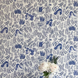 A vase of flowers stands in front of a wall papered in a playful leaf print in shades of blue on a cream field.