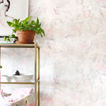 An end table with knick knacks stands in front of a wall papered in an abstract painterly print in pastel, green and cream.