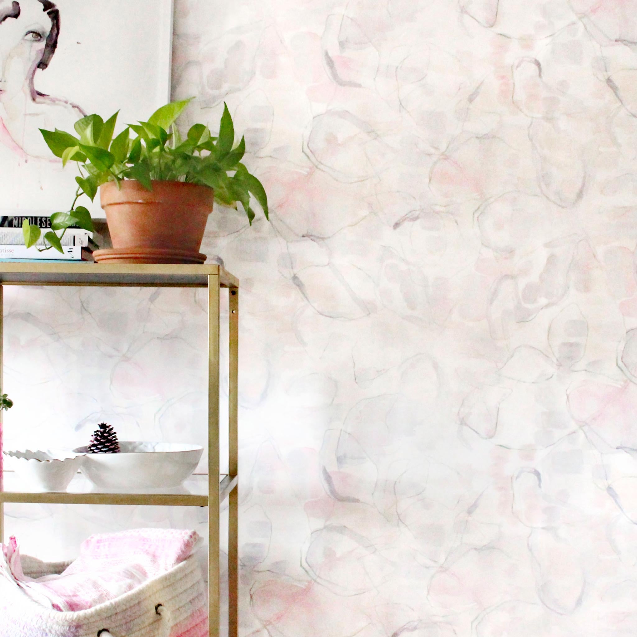 An end table with knick knacks stands in front of a wall papered in an abstract painterly print in pastel, green and cream.