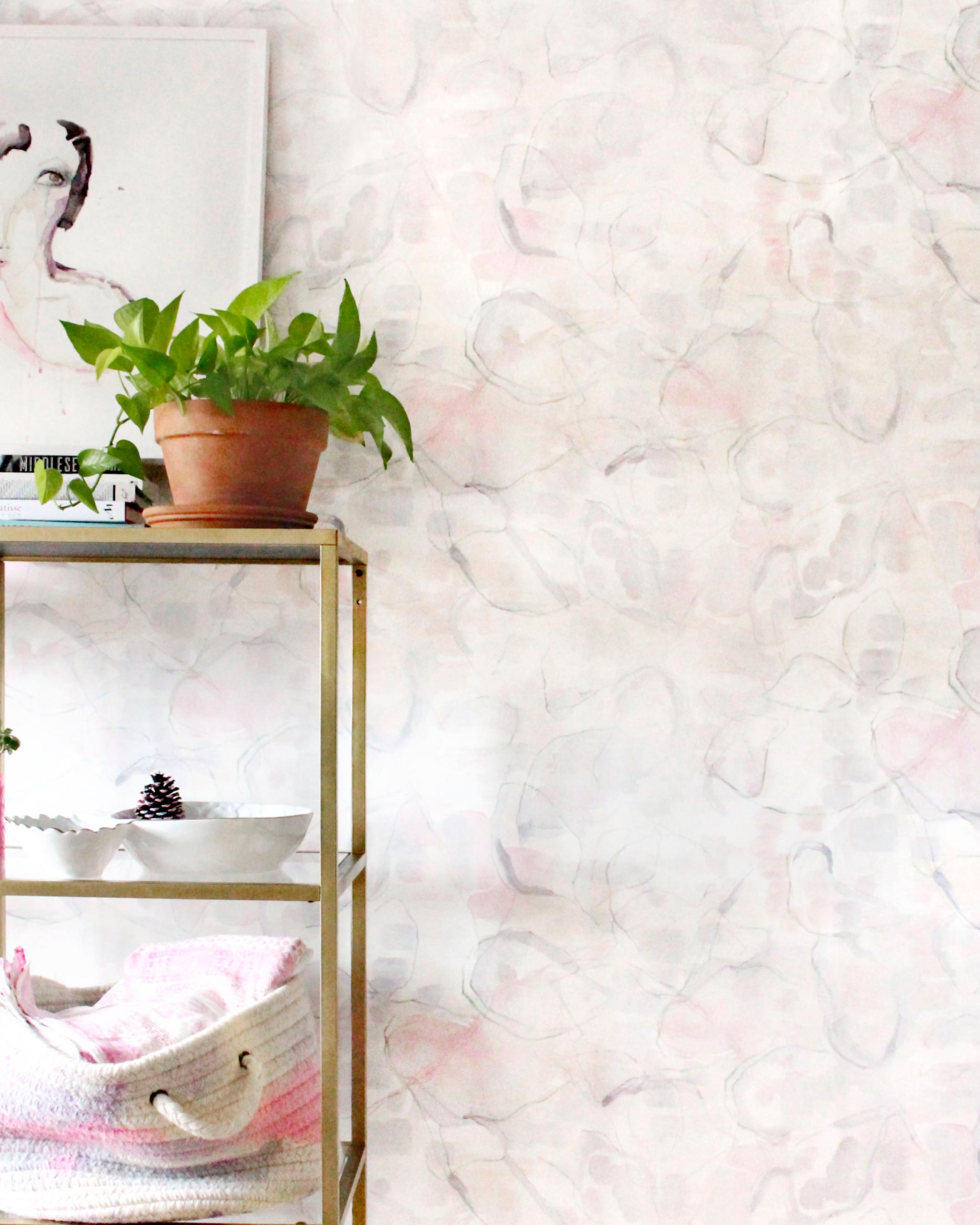 An end table with knick knacks stands in front of a wall papered in an abstract painterly print in pastel, green and cream.