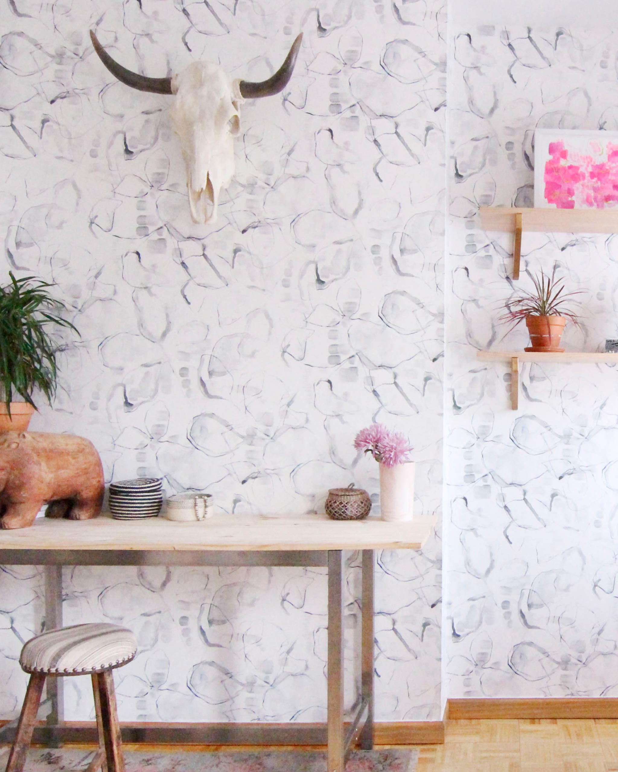 A maximalist living space with walls papered in an abstract painterly print in shades of gray, purple and cream.