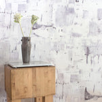 An end table with flowers stands in front of a wall papered in an abstract textural print in shades of gray on a white field.