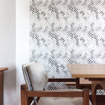 Modernist dining room tableau with a statement wall papered in a painterly chess board print in gray, black and white.