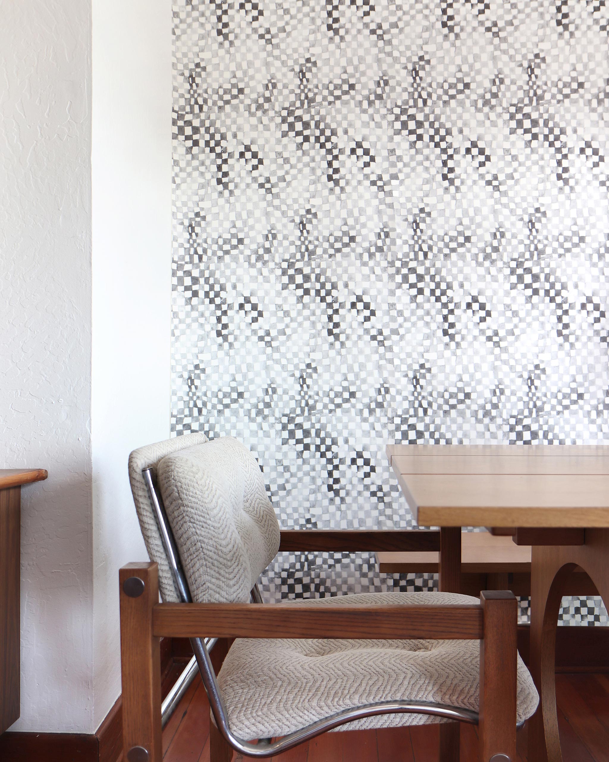 Modernist dining room tableau with a statement wall papered in a painterly chess board print in gray, black and white.