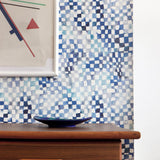 A modernist living tableau with a wall papered in a painterly chess board print in shades of blue, navy and white.