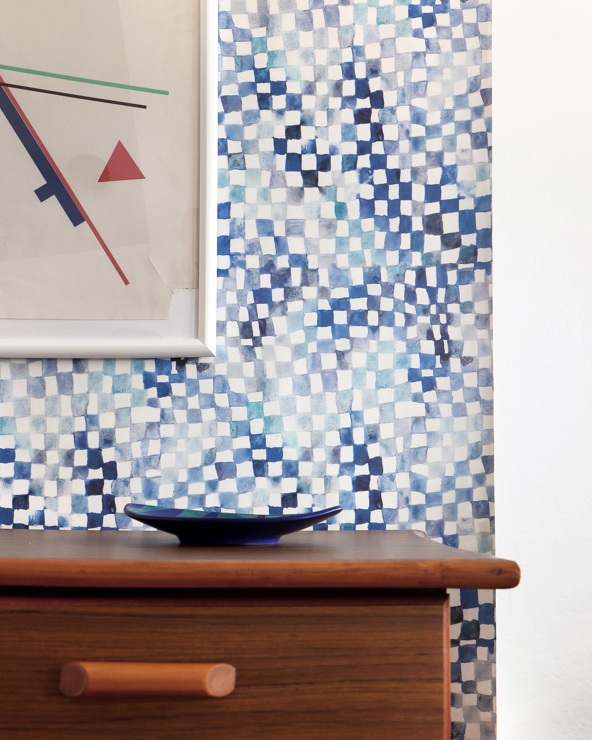 A modernist living tableau with a wall papered in a painterly chess board print in shades of blue, navy and white.