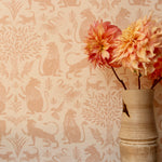 Detail of wallpaper in a lion and plant print in light pink on a white field with a vase with pink flowers.