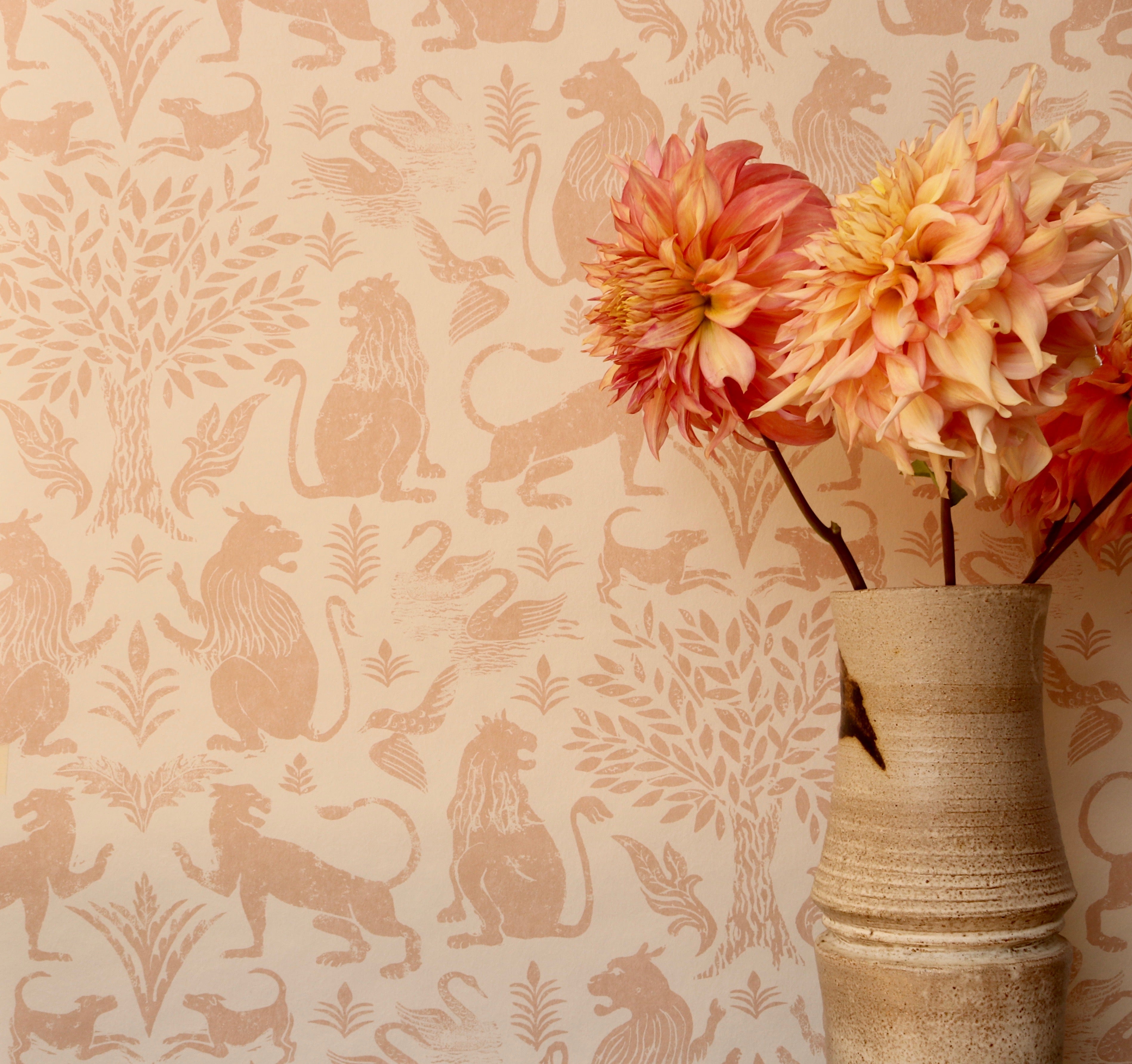 Detail of wallpaper in a lion and plant print in light pink on a white field with a vase with pink flowers.