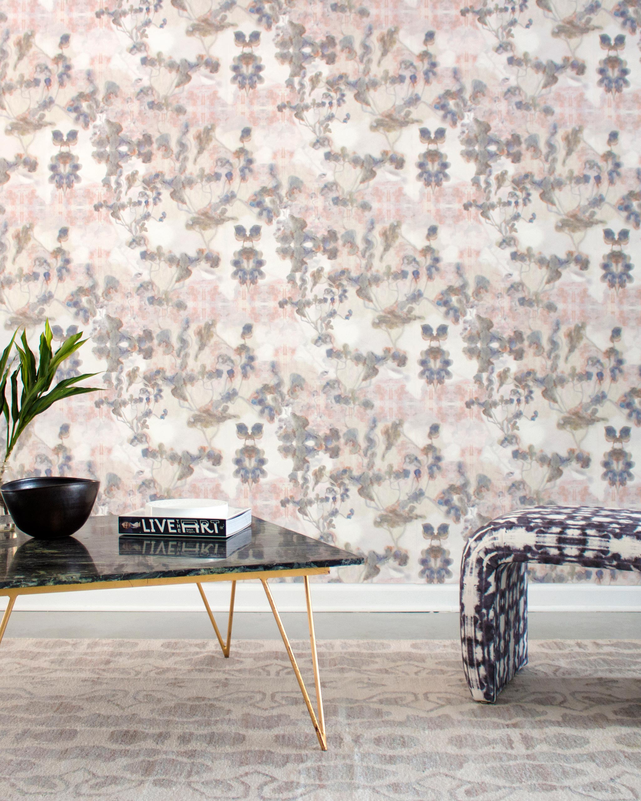 A modernist living tableau with a wall papered in an abstract botanical print in gray, peach, tan and white.