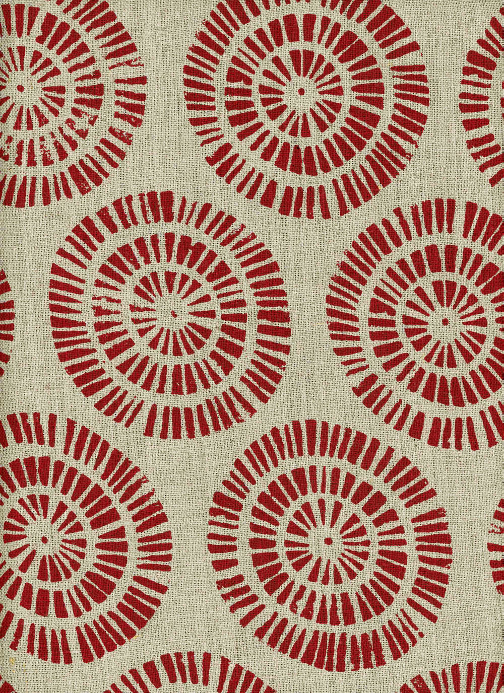 Detail of fabric in a geometric wheel print in red on a tan field.