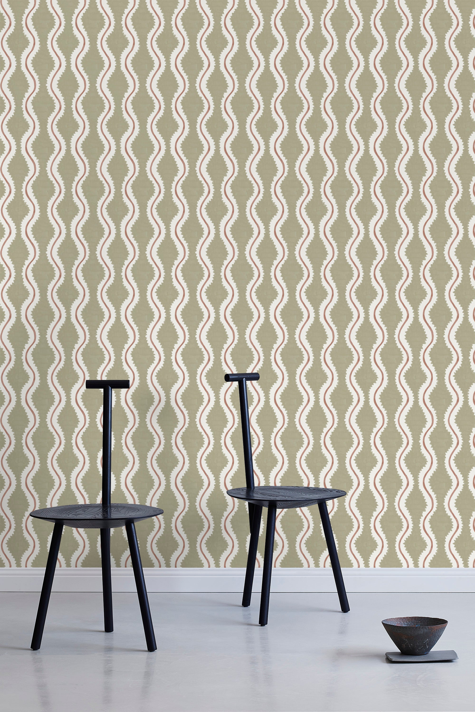 Two minimalist black chairs stand in front of a wall papered in a playful curvy stripe print in white, brown and olive.