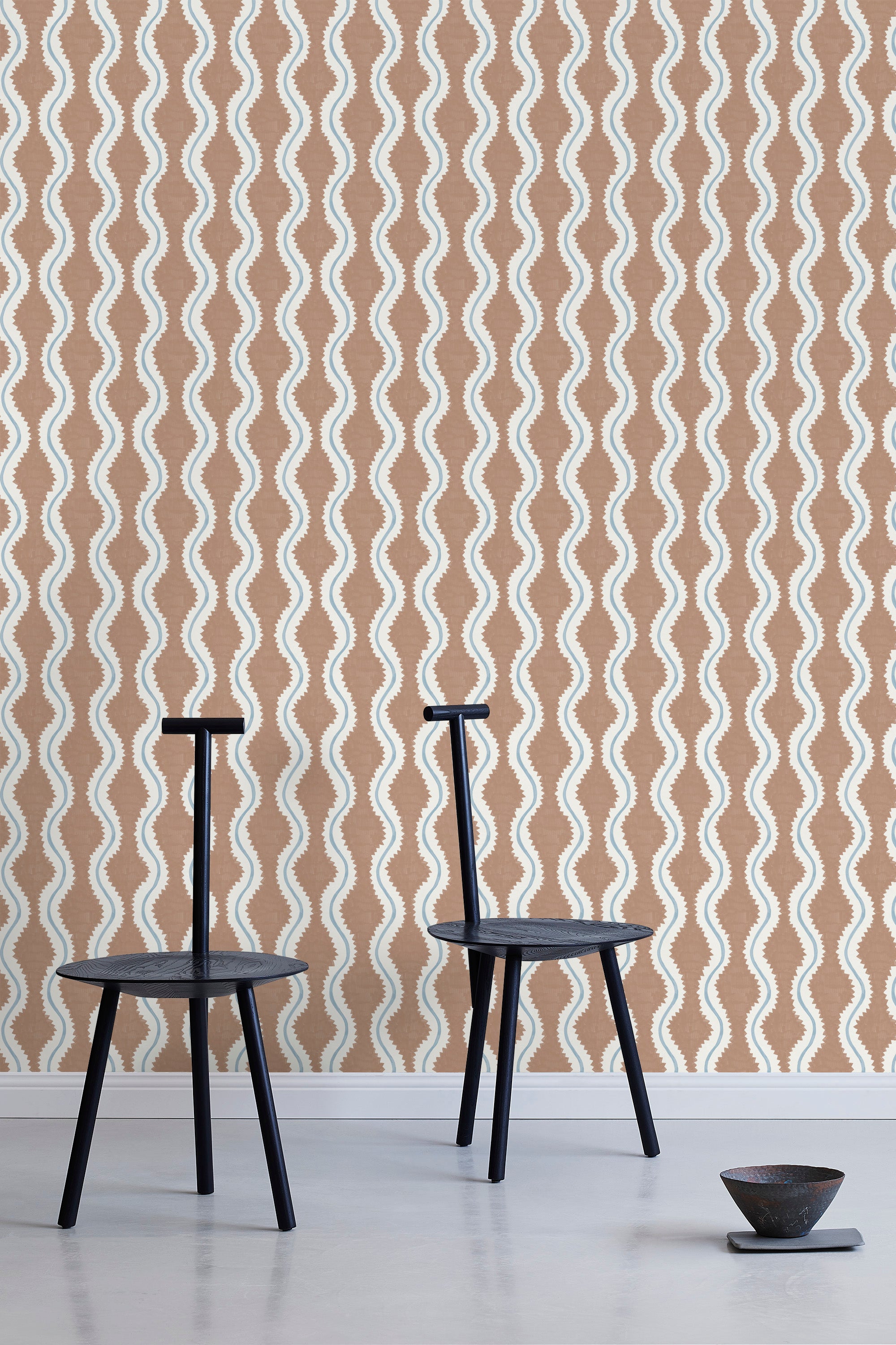 Two minimalist black chairs stand in front of a wall papered in a playful curvy stripe print in white, blue and brown.