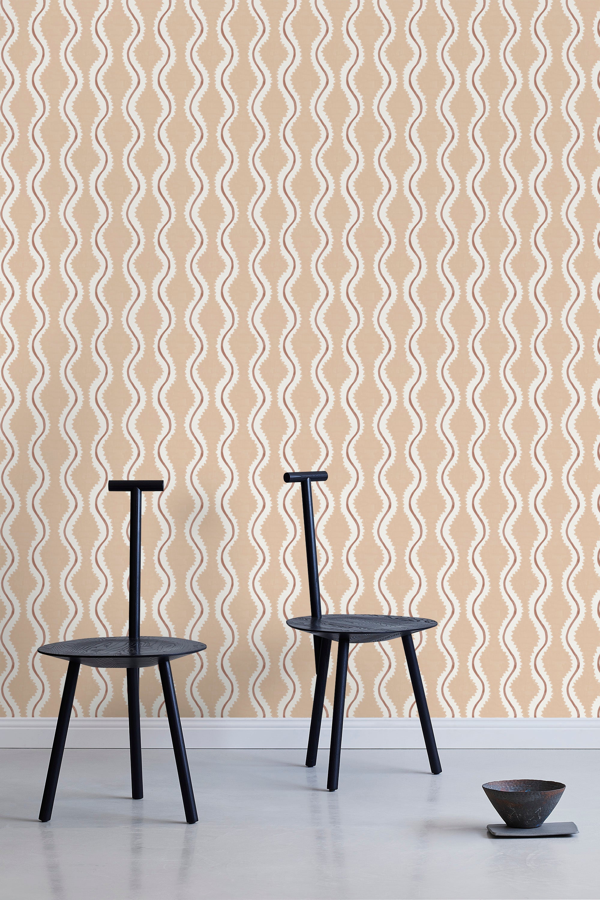 Two minimalist black chairs stand in front of a wall papered in a playful curvy stripe print in white, brown and light pink.