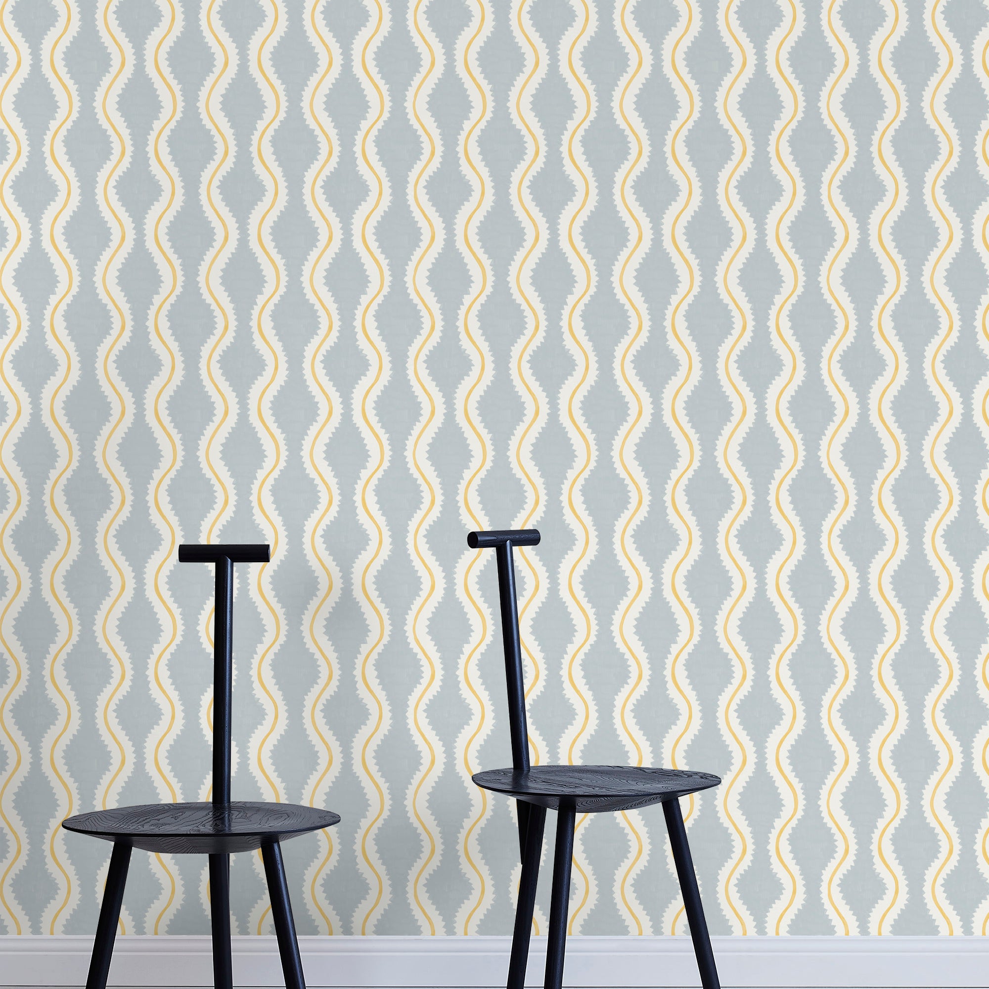 Two minimalist black chairs stand in front of a wall papered in a playful curvy stripe print in white, yellow and light blue.