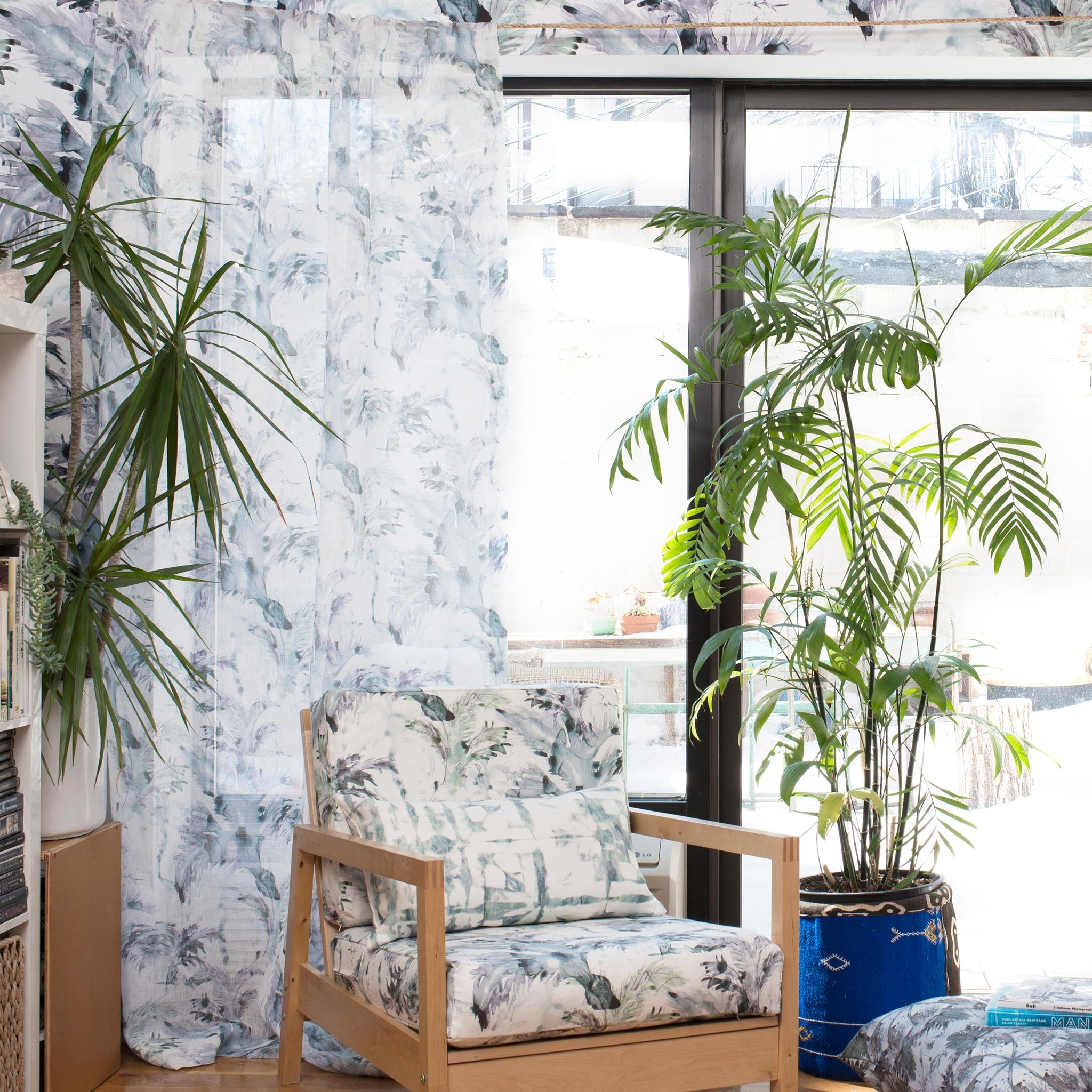 A plant-filled living space with an armchair upholstered in a painterly palm leaf print in turquoise, gray and white.