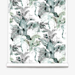 Partially unrolled wallpaper yardage in a painterly palm tree print in shades of gray, blue and green on a white field.