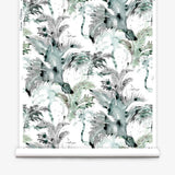 Partially unrolled wallpaper yardage in a painterly palm tree print in shades of gray, blue and green on a white field.