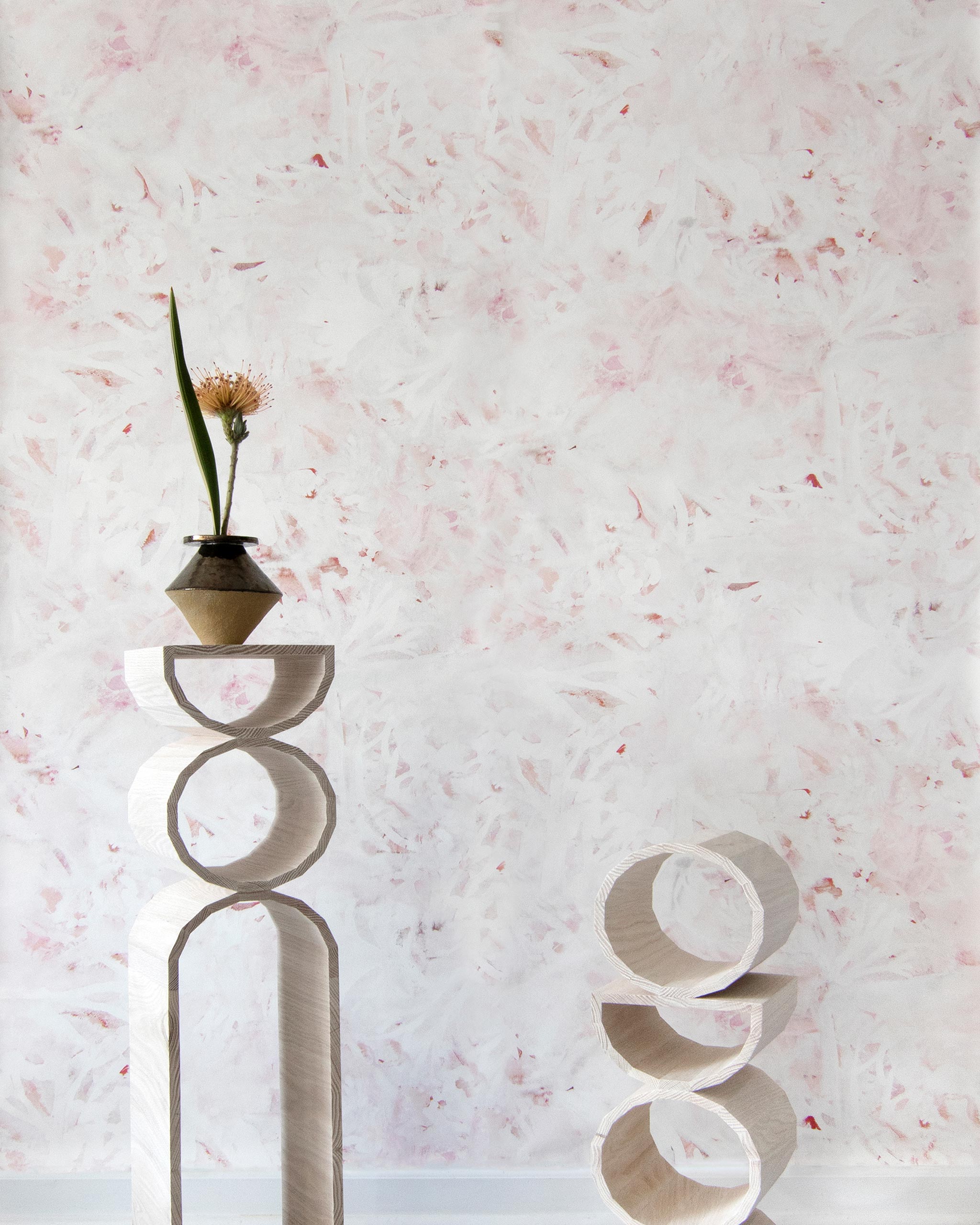 Modernist end tables stand in front of a wall papered in an abstract painted print in shades of pink, red and white.