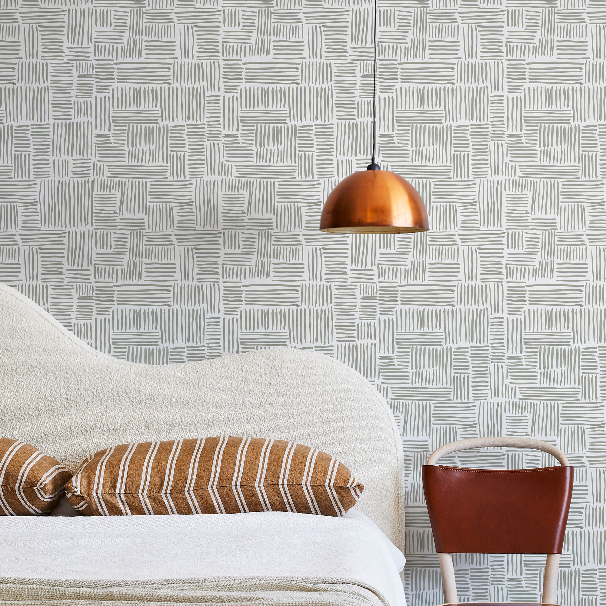 A modernist bed, hanging lamp and chair stand in front of a wall papered in a directional dash pattern in green-gray and white.