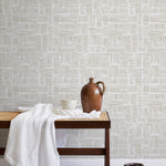 A bench with a towel and clay vases stands in front of a wall papered in a directional dash pattern in cream and white.