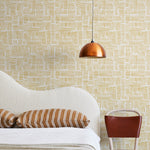 A modernist bed, hanging lamp and chair stand in front of a wall papered in a directional dash pattern in yellow and white.