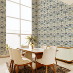 A modernist dining room with a tall window and walls papered in a floral damask print in navy, cream and gold.