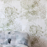 A bed stands in front of a wall papered in a painterly palm tree print in olive on a cream field.