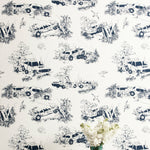 A vase of flowers stands in front of a wall covered in a playful illustrated car crash print in navy on a white field.