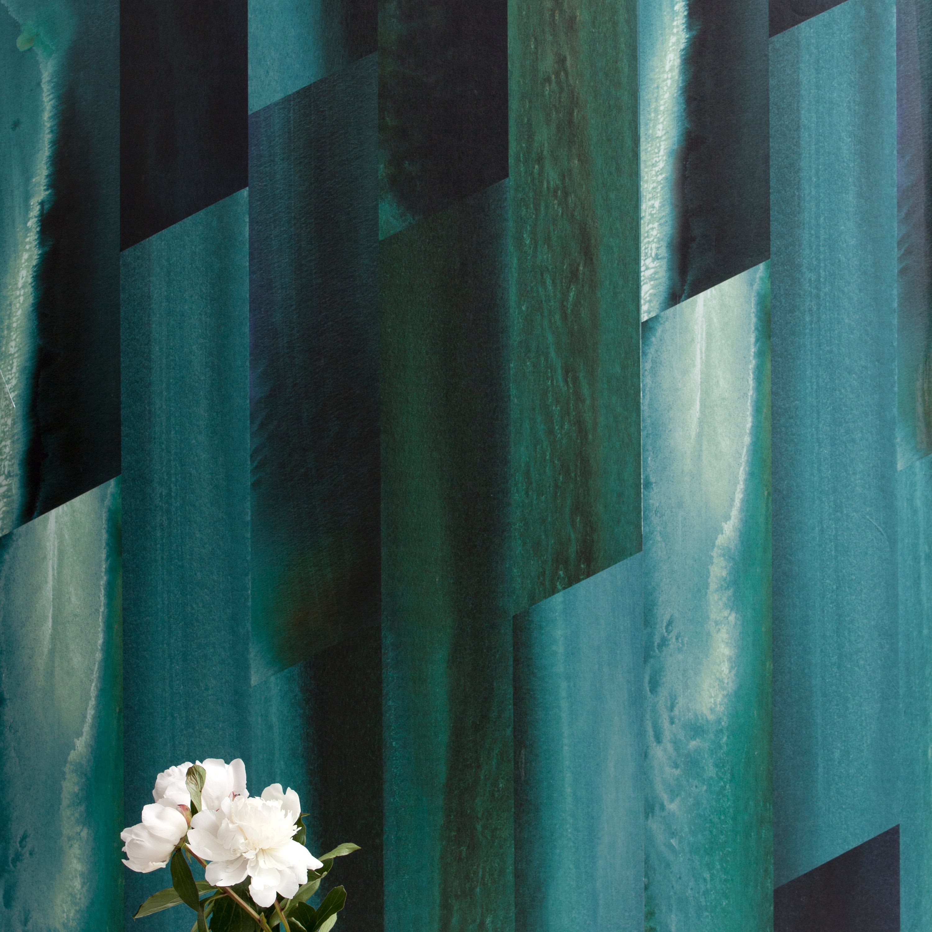 A vase of flowers stands in front of a wall papered in a linear geometric print in shades of black, blue and turquoise.